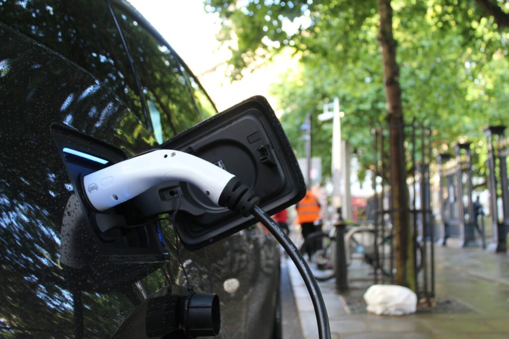 An electric car being charged on a leafy street